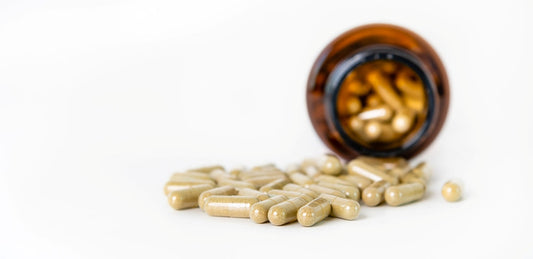 Herbal medicine capsules spilling out of a bottle on white background