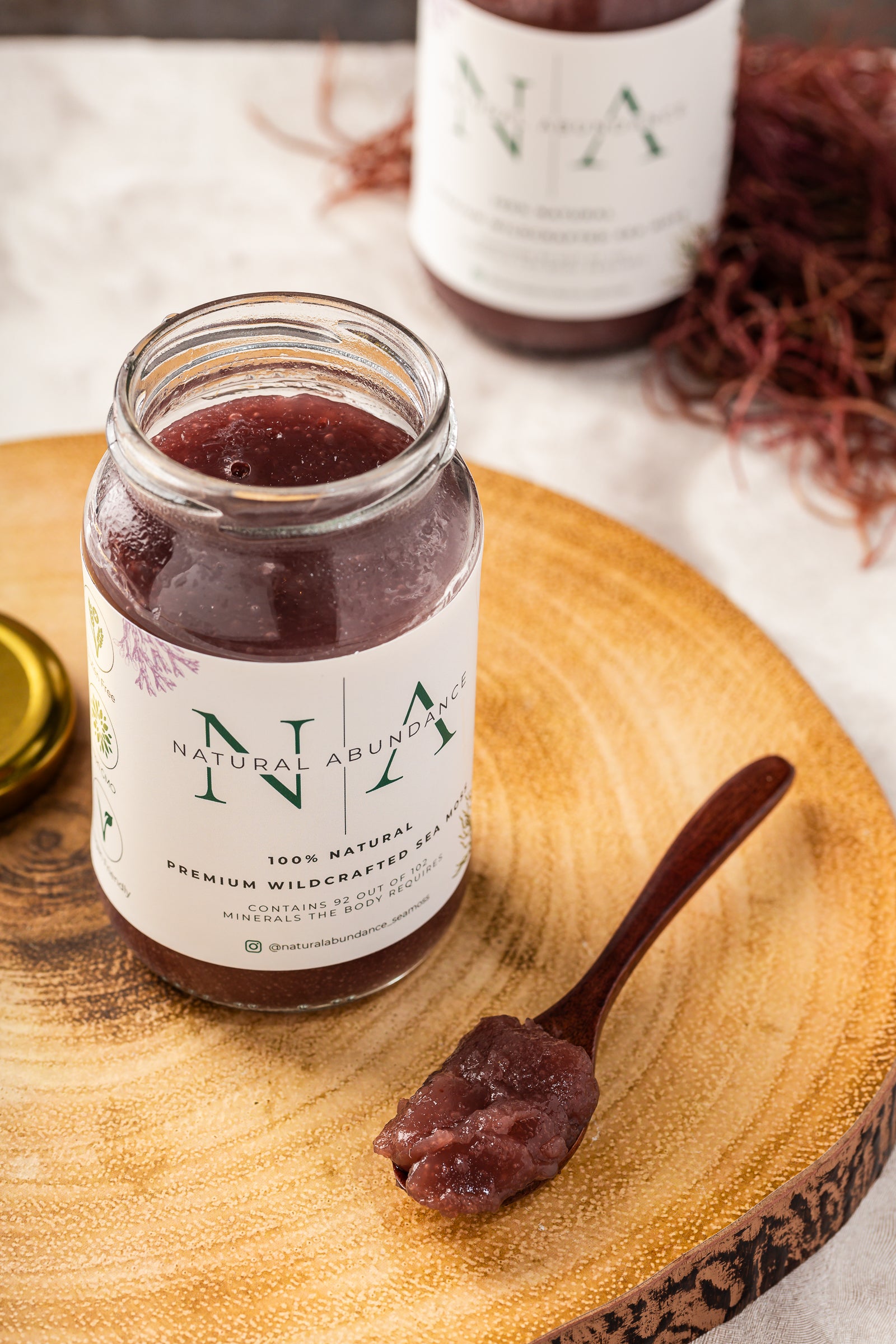 Four jars of Natural Abundance Premium Wildcrafted Sea Moss placed on a marble surface with lemon, lime, and sea moss strands for decoration.