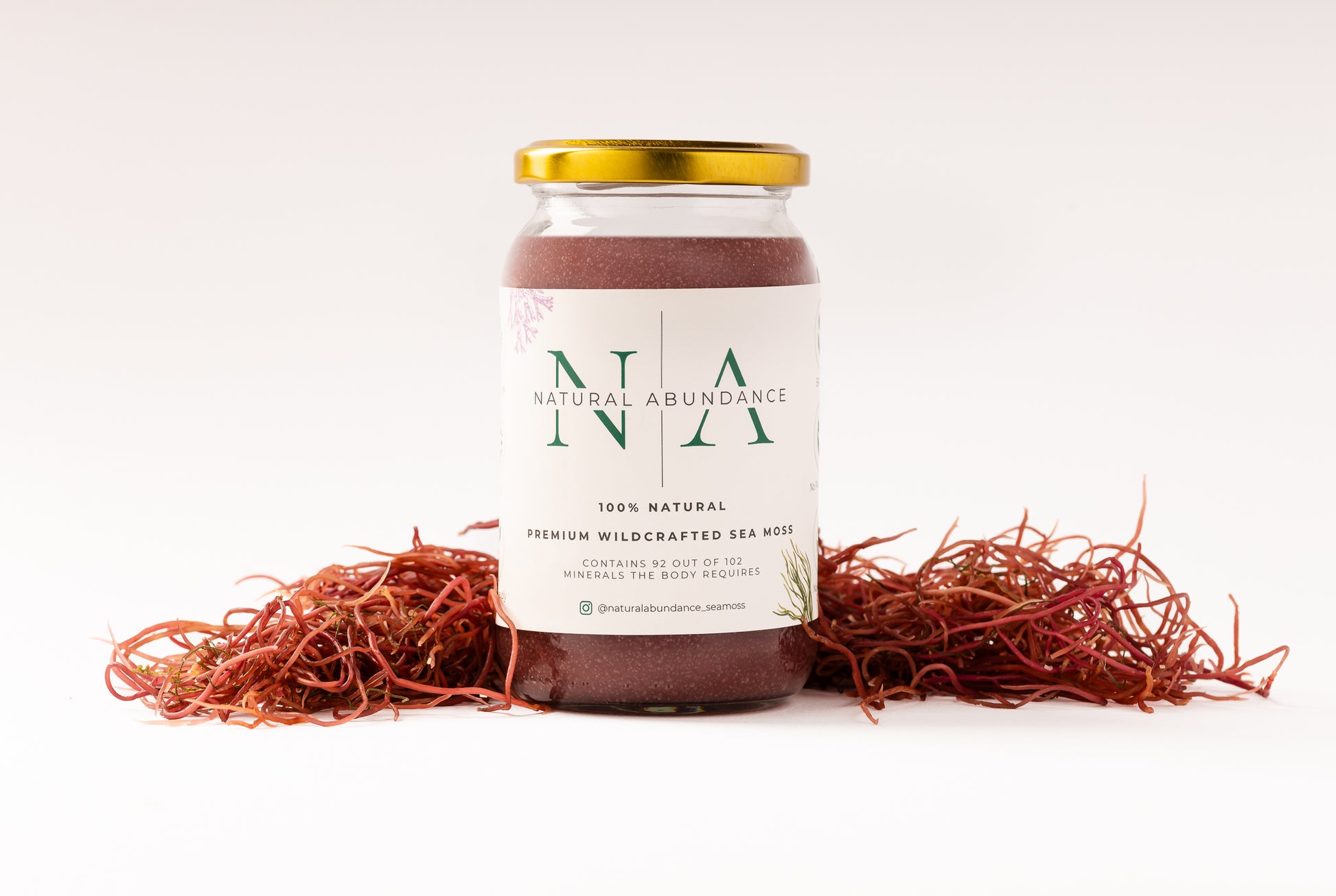 Jar of Natural Abundance 100% natural premium wildcrafted sea moss with gold lid, placed on white background surrounded by dried red sea moss.