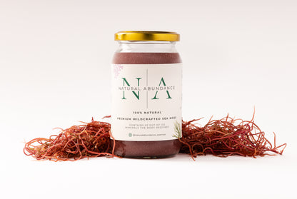 Jar of Natural Abundance 100% natural premium wildcrafted sea moss with gold lid, placed on white background surrounded by dried red sea moss.